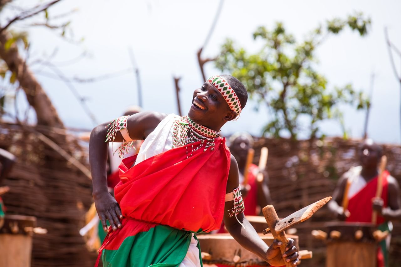Smiling man in vibrant traditional attire performs a tribal dance outdoors.